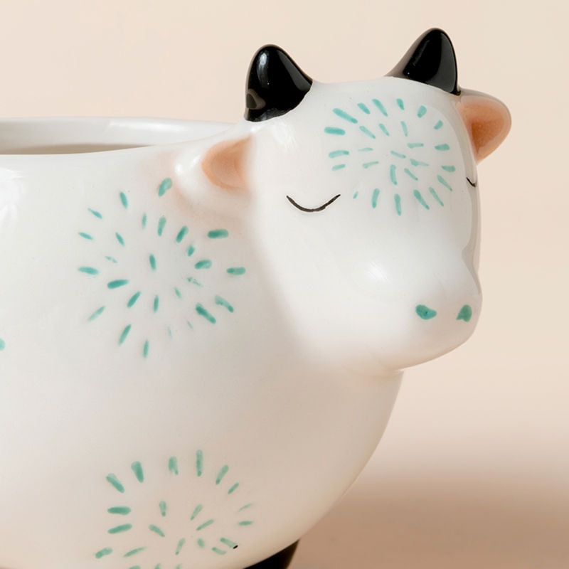 A close-up of the cow-shaped small pots. The planter is made of ceramic and decorated with blue fireworks shape.