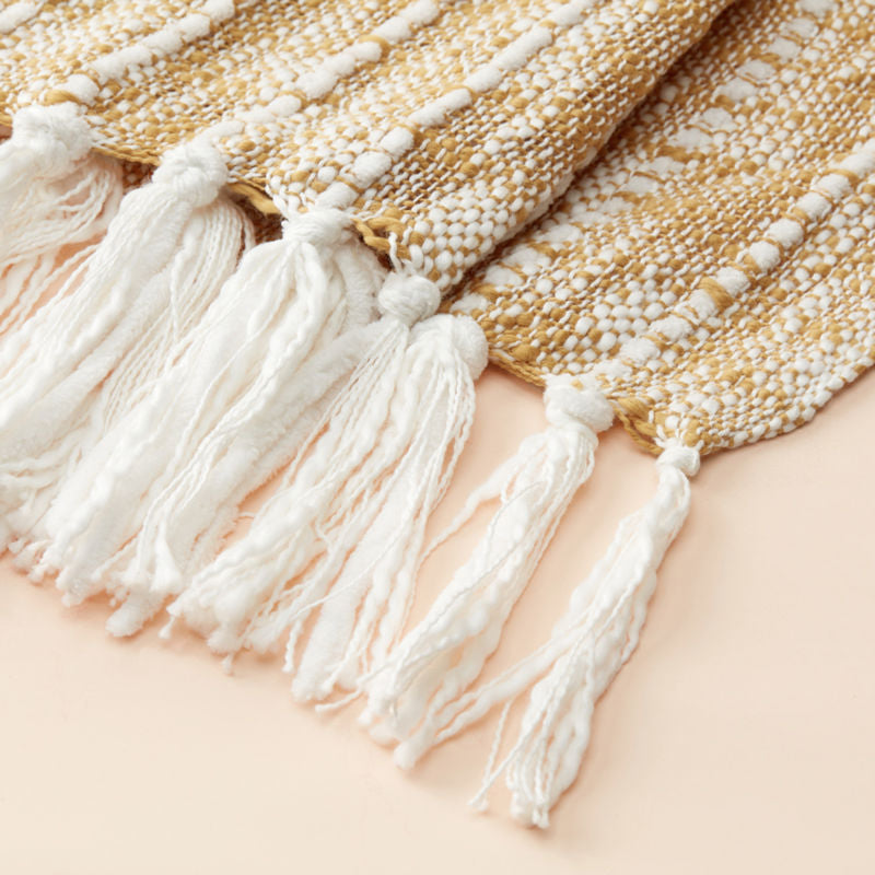The close-up shows the end knots of the white and yellow throw blanket made softly with cotton.
